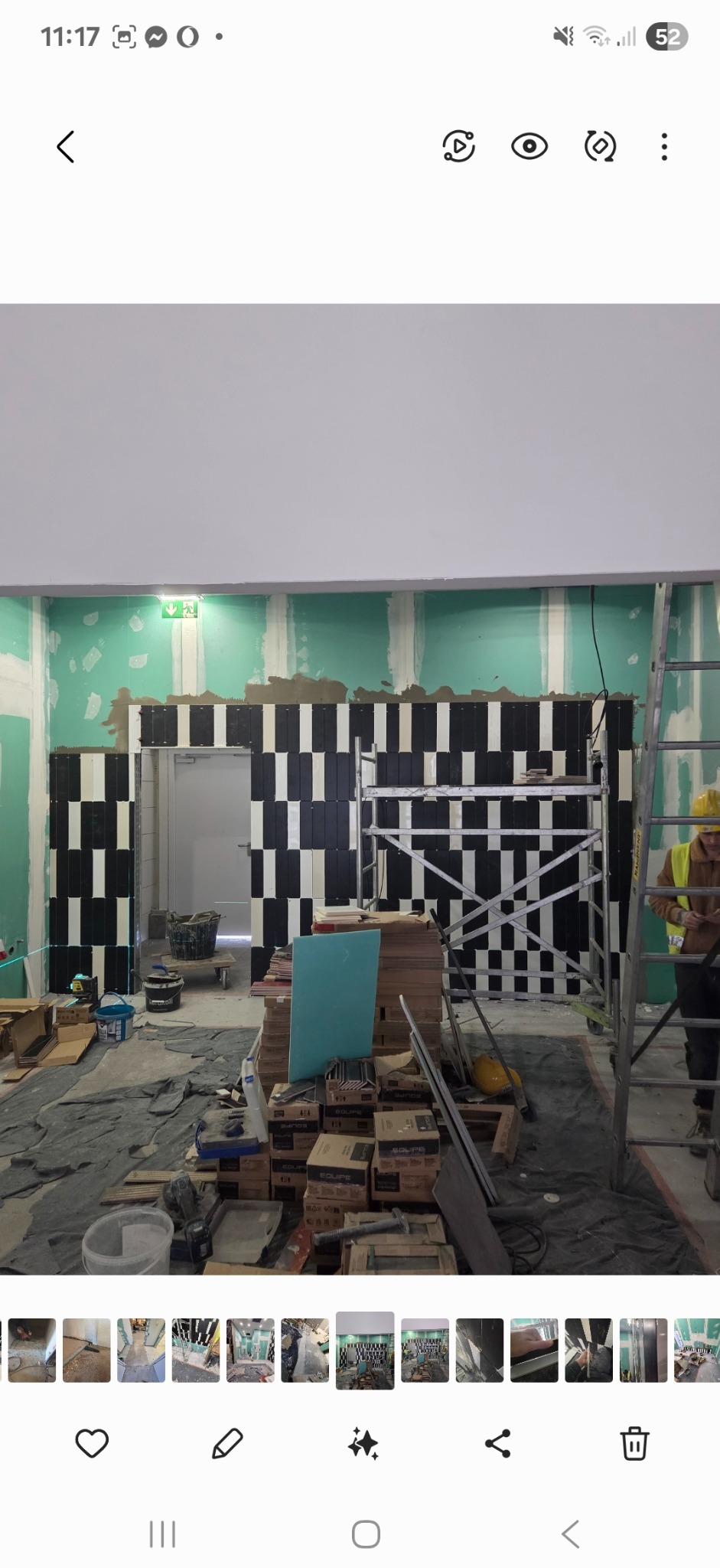 Układanie czarno-białych płytek na ścianie w pionowe pasy. Widoczne rusztowanie i narzędzia glazurnicze. Prace w toku, surowy stan.