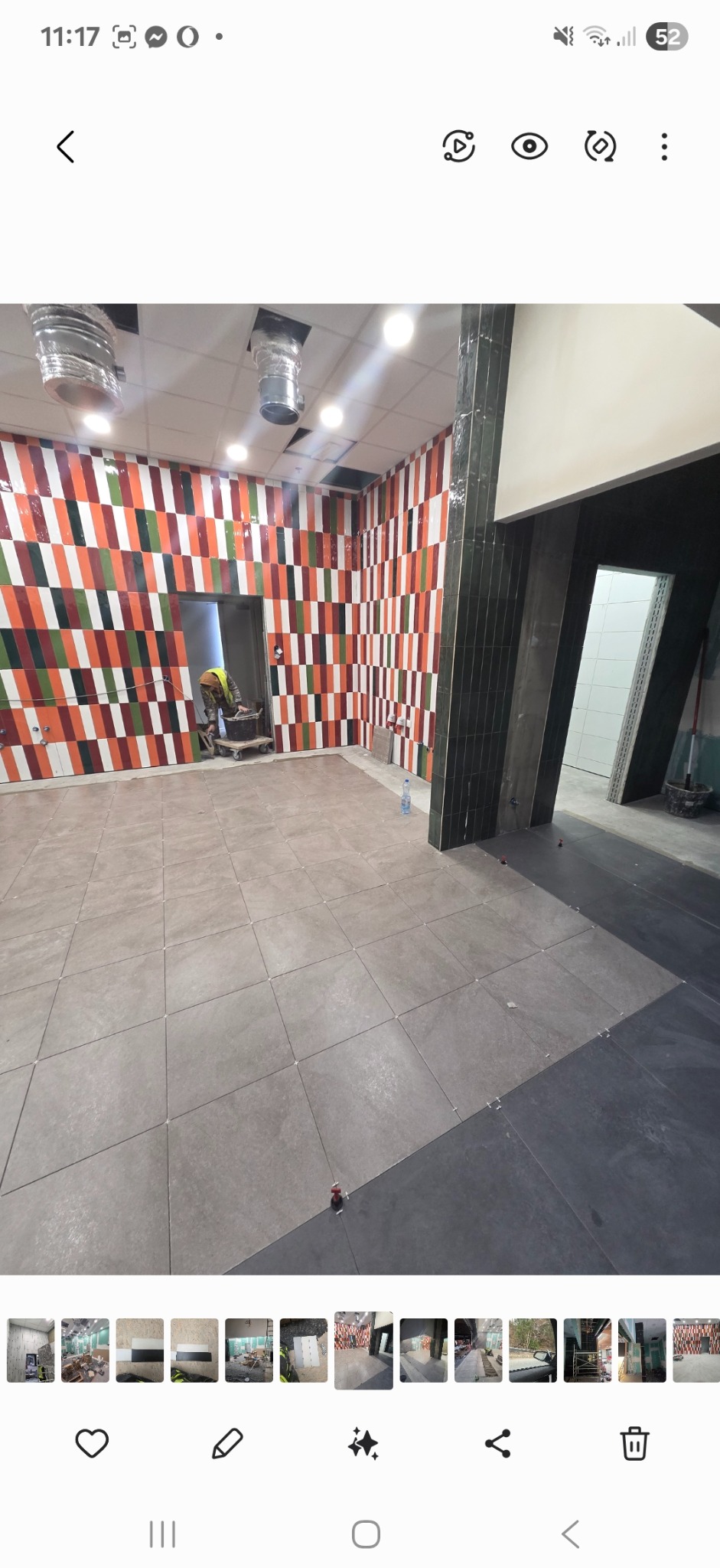 Wnętrze w trakcie prac glazurniczych: ułożone płytki podłogowe i wzorzyste płytki ścienne w odcieniach czerwieni, pomarańczy, zieleni i bieli. Widoczny pracownik w tle.