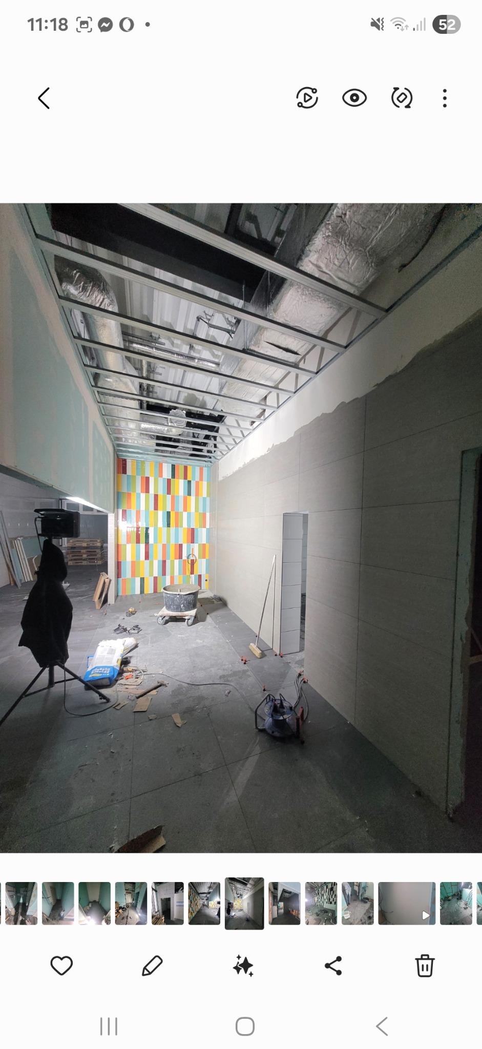 Wnętrze w trakcie prac wykończeniowych: ułożona szara podłoga, częściowo położone płytki na ścianach, kolorowa ściana z płytek. Widoczne narzędzia i materiały budowlane.