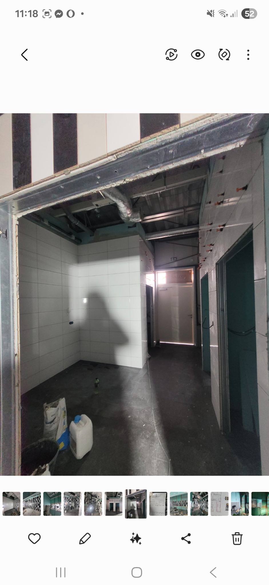 Wnętrze w trakcie wykańczania: białe płytki na ścianach, widoczne worki z zaprawą, elementy instalacji pod sufitem. Prace glazurnicze w toku, widoczny system poziomowania płytek.