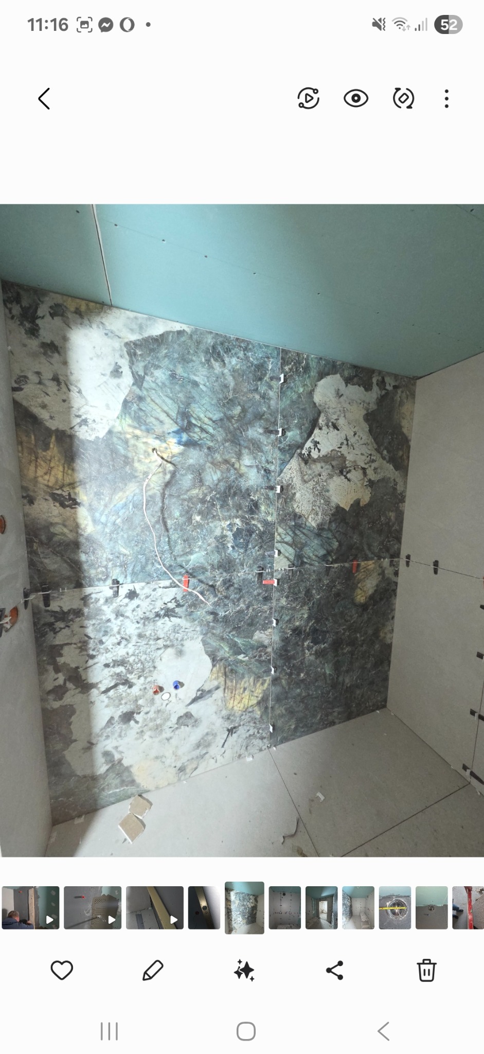 Układanie płytek z marmurkowym wzorem na ścianie łazienki. Widoczne krzyżyki dystansowe i wystające kable. Częściowo wykończone ściany i sufit z płyty gipsowej.