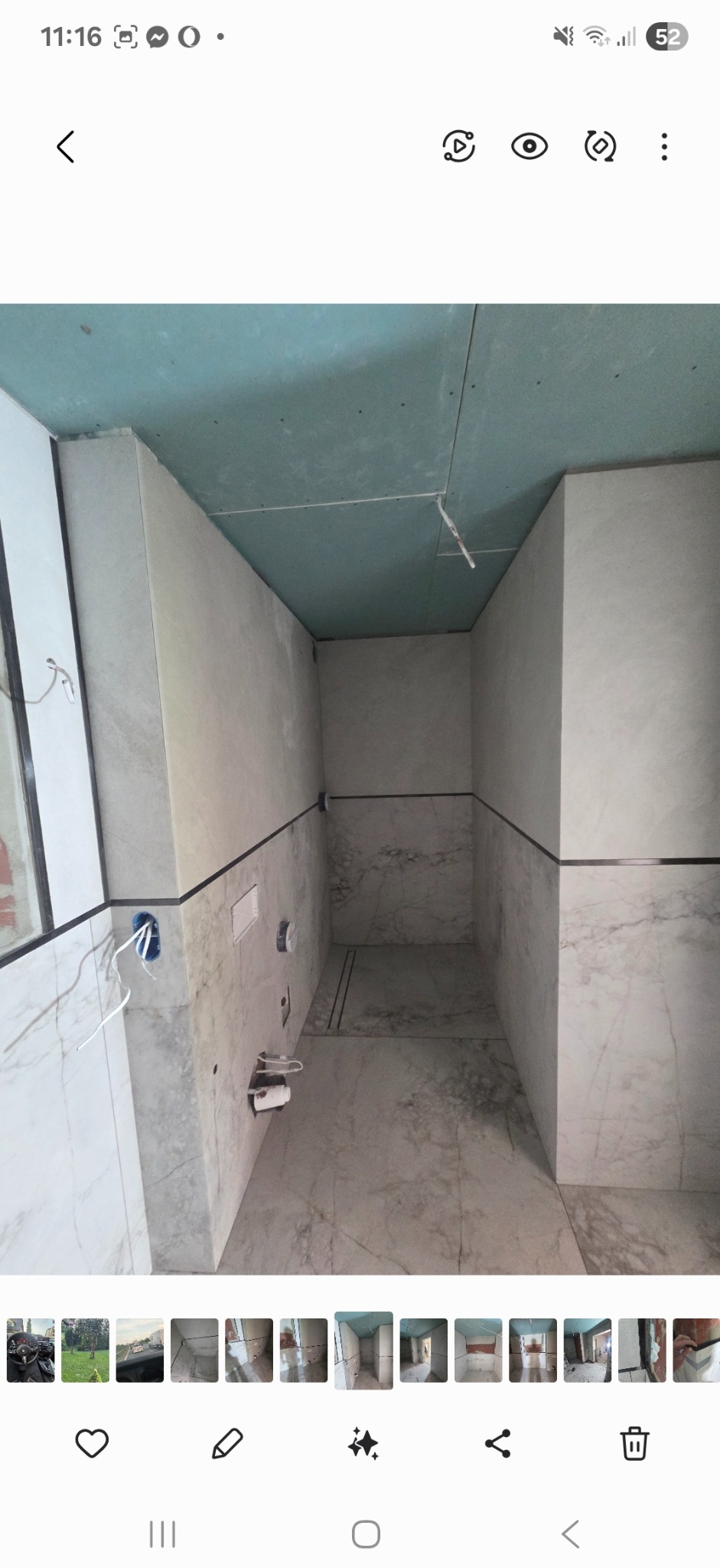 Wnętrze łazienki w trakcie wykańczania. Ściany i podłoga wyłożone płytkami imitującymi marmur. Sufit z płyt kartonowo-gipsowych. Widoczne instalacje.