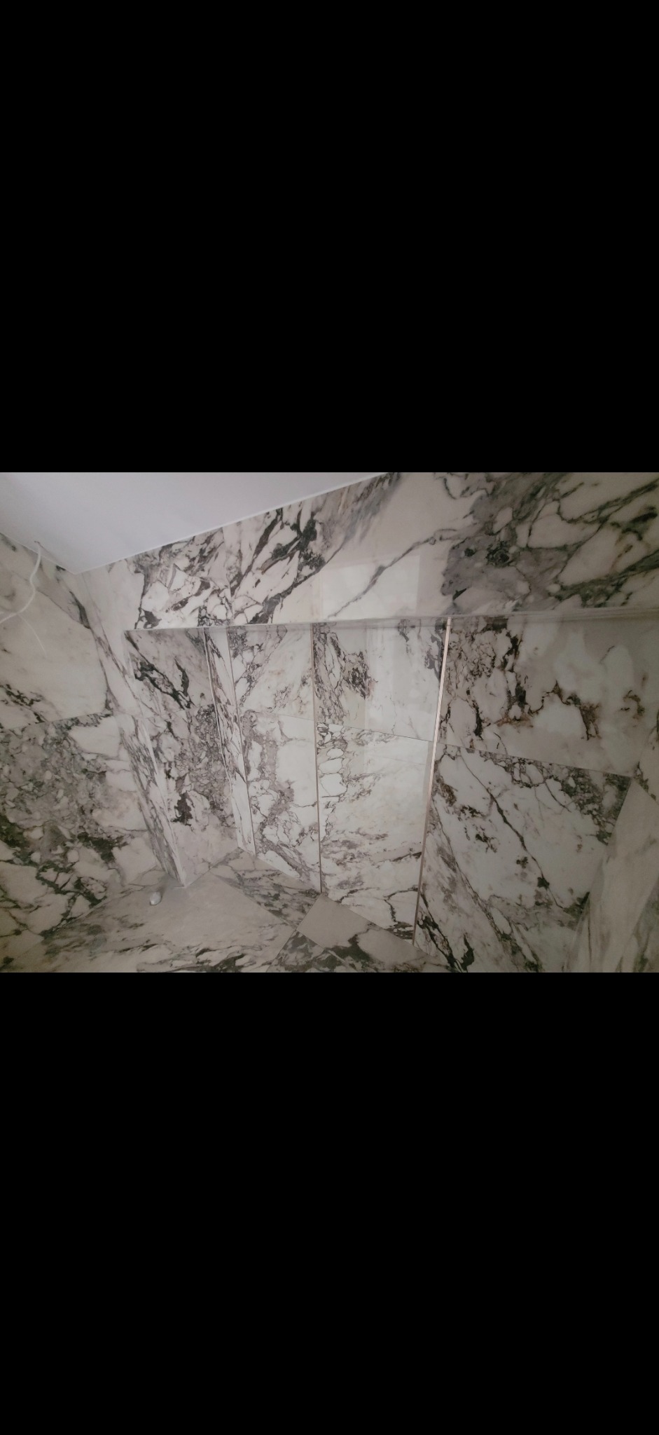 Wykończona łazienka z płytkami imitującymi marmur na ścianach i podłodze. Płytki ułożone w pionie, widoczne fugi. Biały sufit.