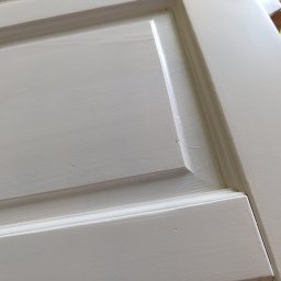 S&M BEST - Fragment świeżo pomalowanych na szaro drzwi panelowych z widoczną fakturą pędzla, uchwycony pod kątem z bliska, prezentujący detale wykończenia.