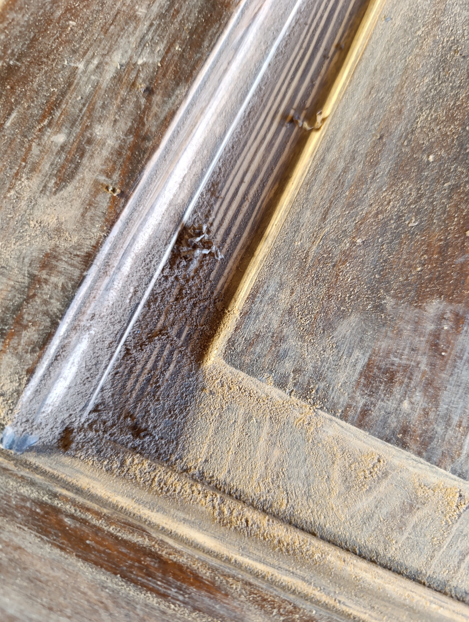 Szczegółowe ujęcie drewnianych drzwi z wyraźnymi śladami pyłu po szlifowaniu, ukazujące proces renowacji i dbałość o detale podczas odświeżania powierzchni.