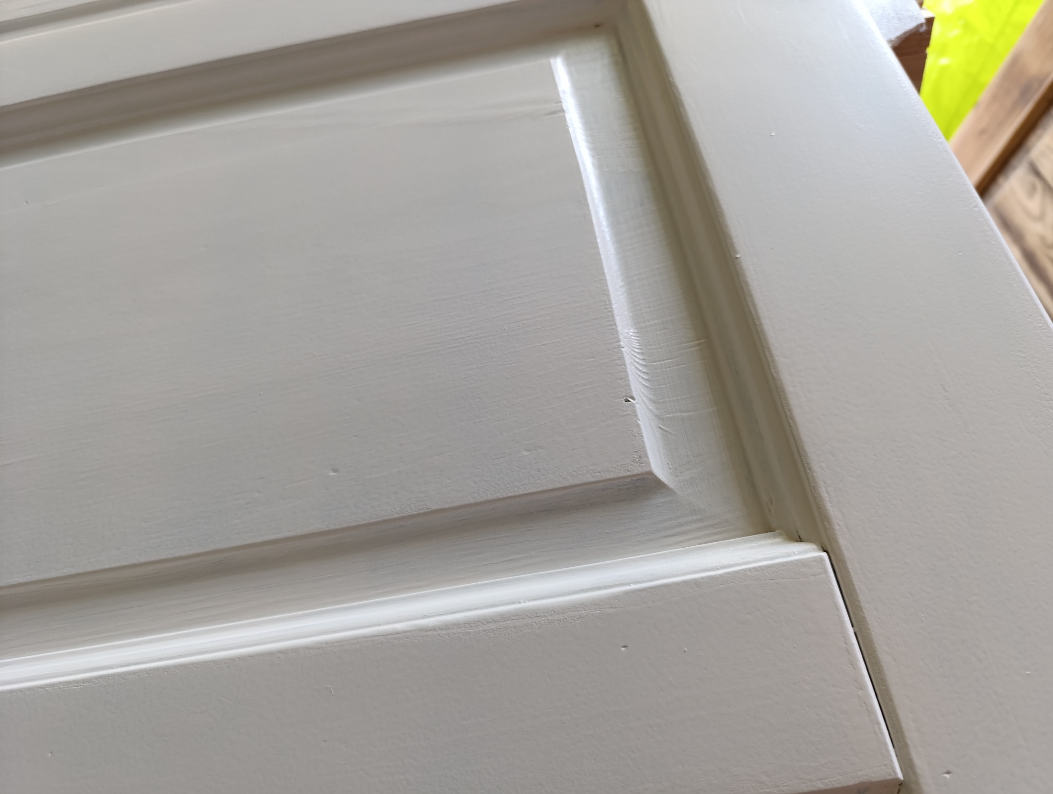 Fragment świeżo pomalowanych na szaro drzwi panelowych z widoczną fakturą pędzla, uchwycony pod kątem z bliska, prezentujący detale wykończenia.