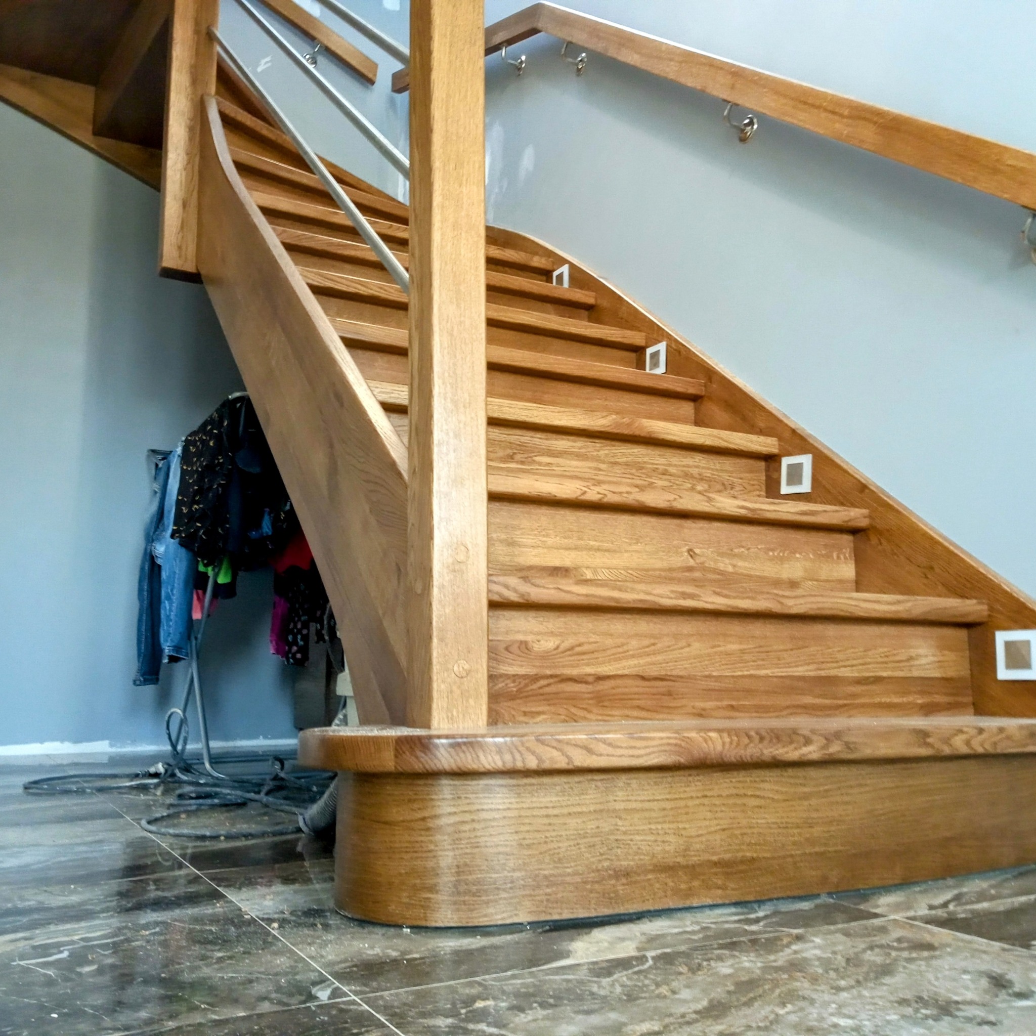 Nowoczesne schody z drewna dębowego z metalową balustradą i podświetleniem LED, widok z dołu, ukazujący detale wykończenia i strukturę drewna.