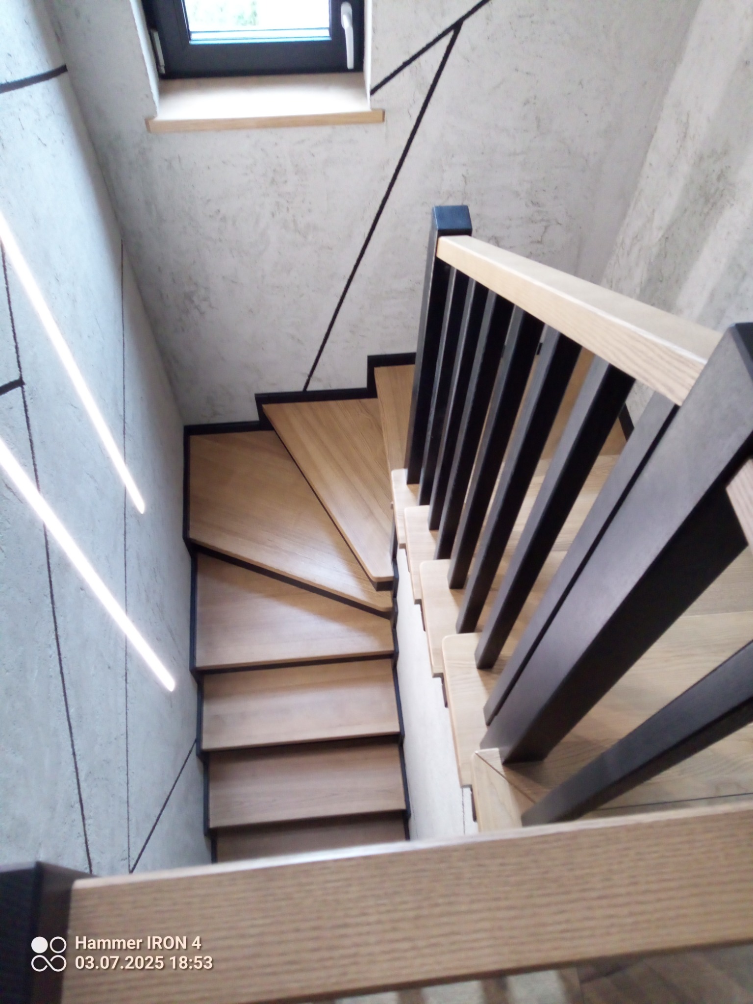 Nowoczesne schody z jasnego drewna z czarnymi elementami, widok z góry. Ściana z dekoracyjnym wzorem i oknem dachowym. Minimalistyczny design.