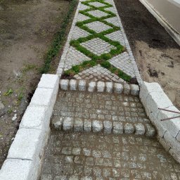 Waldek tobiaski - Ścieżka z kostki granitowej z elementami zieleni, tworząca geometryczny wzór. Widoczne stopnie z kostki i obrzeża, świeżo ułożona, jasna kostka.