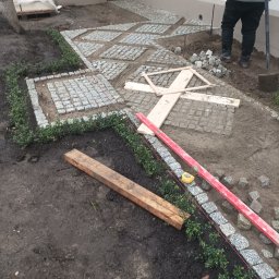 Waldek tobiaski - Układanie kostki granitowej w geometryczny wzór, obrzeża z bukszpanu i kostki. Widoczne narzędzia: poziomica, szpadel, drewniane stemple. Prace w toku.