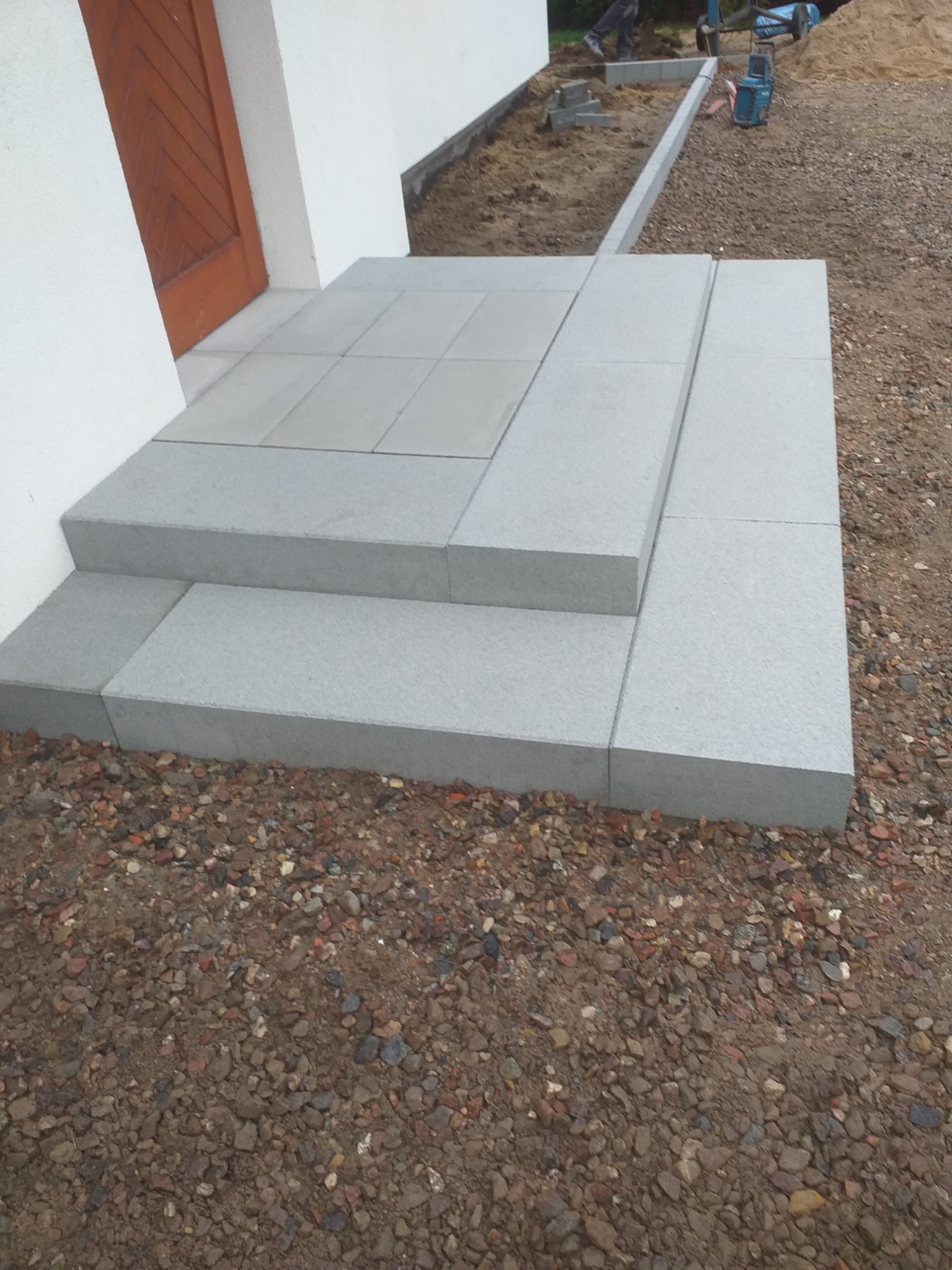 Schody wejściowe z jasnoszarej kostki granitowej, prowadzące do drzwi w Grabowie Kościerskim. Otoczenie w trakcie prac wykończeniowych.