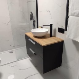 Projekt Wnętrz Sebastian Burski - Nowoczesna łazienka z kabiną prysznicową typu walk-in, umywalką nablatową na szafce z drewnianym blatem i białymi płytkami imitującymi marmur.