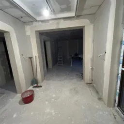 Wnętrze w trakcie prac wykończeniowych: ściany z płyt karton-gips, surowy beton na podłodze, widoczne narzędzia i drabina w głębi. Okno z logo Veka.