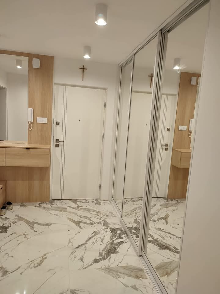 Nowoczesny przedpokój z lustrzaną szafą przesuwną, marmurową podłogą i drewnianymi elementami. Minimalistyczny design, jasne oświetlenie punktowe.