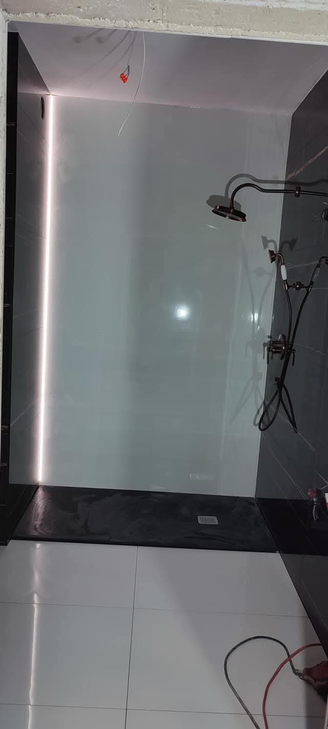 Nowoczesna kabina prysznicowa z deszczownicą, czarno-białymi płytkami i podświetleniem LED. Widoczne kable elektryczne w suficie, sugerujące etap wykończenia.