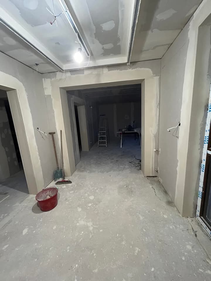 Wnętrze w trakcie prac wykończeniowych: ściany z płyt karton-gips, surowy beton na podłodze, widoczne narzędzia i drabina w głębi. Okno z logo Veka.