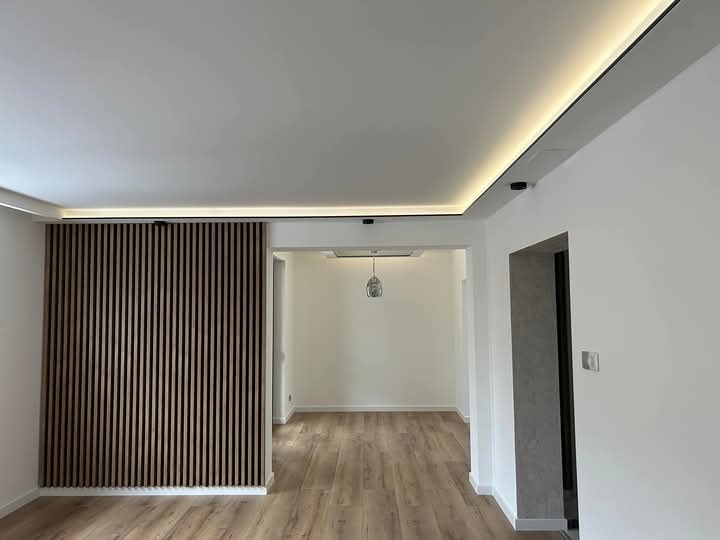 Nowoczesne wnętrze: drewniana ścianka działowa z listew, podświetlony sufit i parkiet. Minimalistyczny design z otwartym przejściem do kolejnego pomieszczenia.