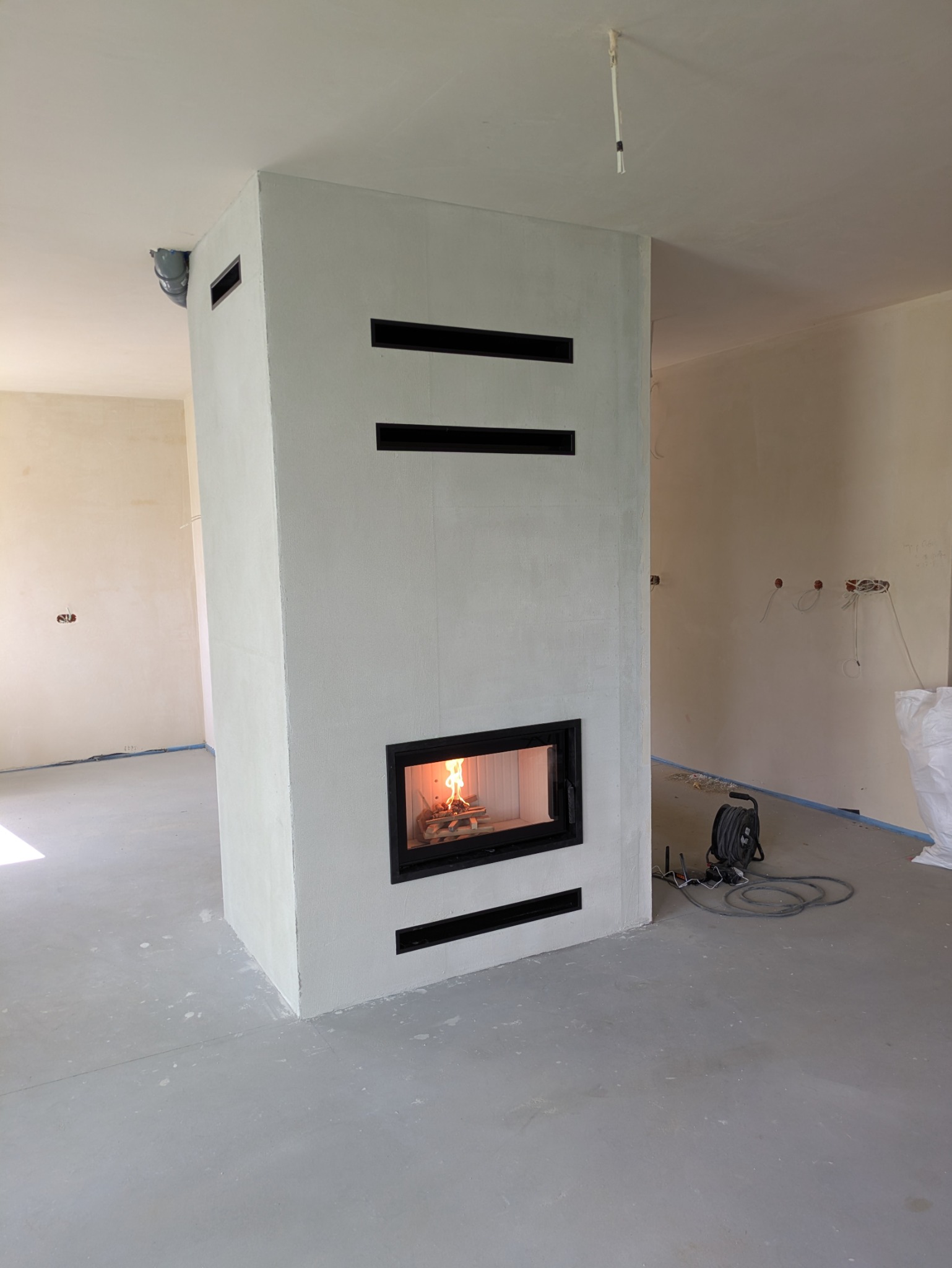 Nowoczesny kominek z wkładem i obudową w trakcie wykończenia w Niedrzwicy Dużej. Widoczne szczeliny wentylacyjne i przewody instalacyjne.