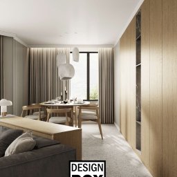 DESIGNBOX - Stylowa aranżacja wnętrza z drewnianą zabudową, okrągłym stołem i nowoczesnymi lampami wiszącymi. Stonowana kolorystyka, minimalistyczny design, widok na zieleń za oknem.