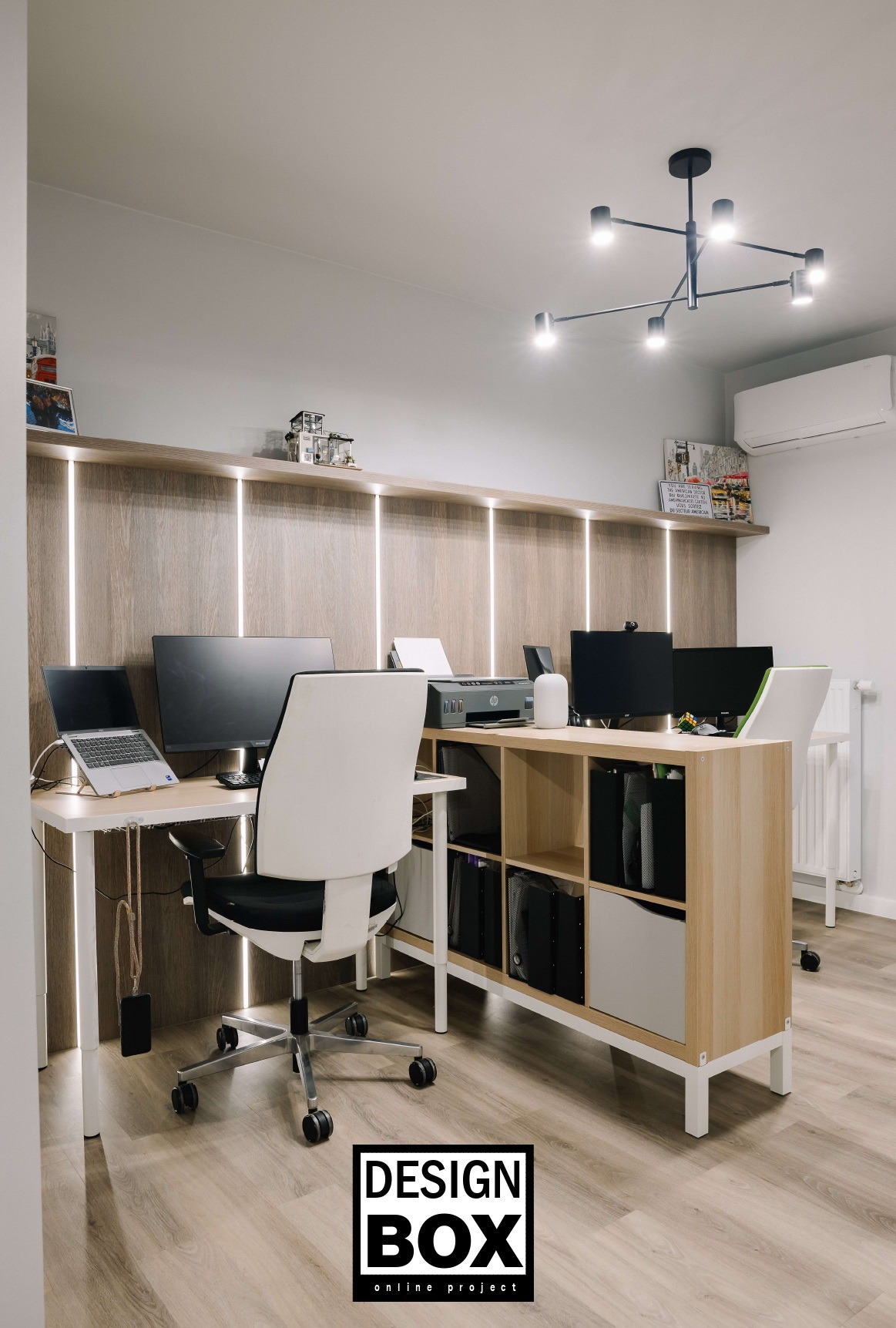 Nowoczesne biuro domowe z dwoma stanowiskami, drewnianymi akcentami i oświetleniem LED. Laptop, monitory, drukarka i ergonomiczne krzesła tworzą funkcjonalną przestrzeń.