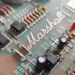 Zbliżenie na płytkę drukowaną Marshall z elementami elektronicznymi, takimi jak rezystory i układy scalone, z wyraźnym napisem marki.