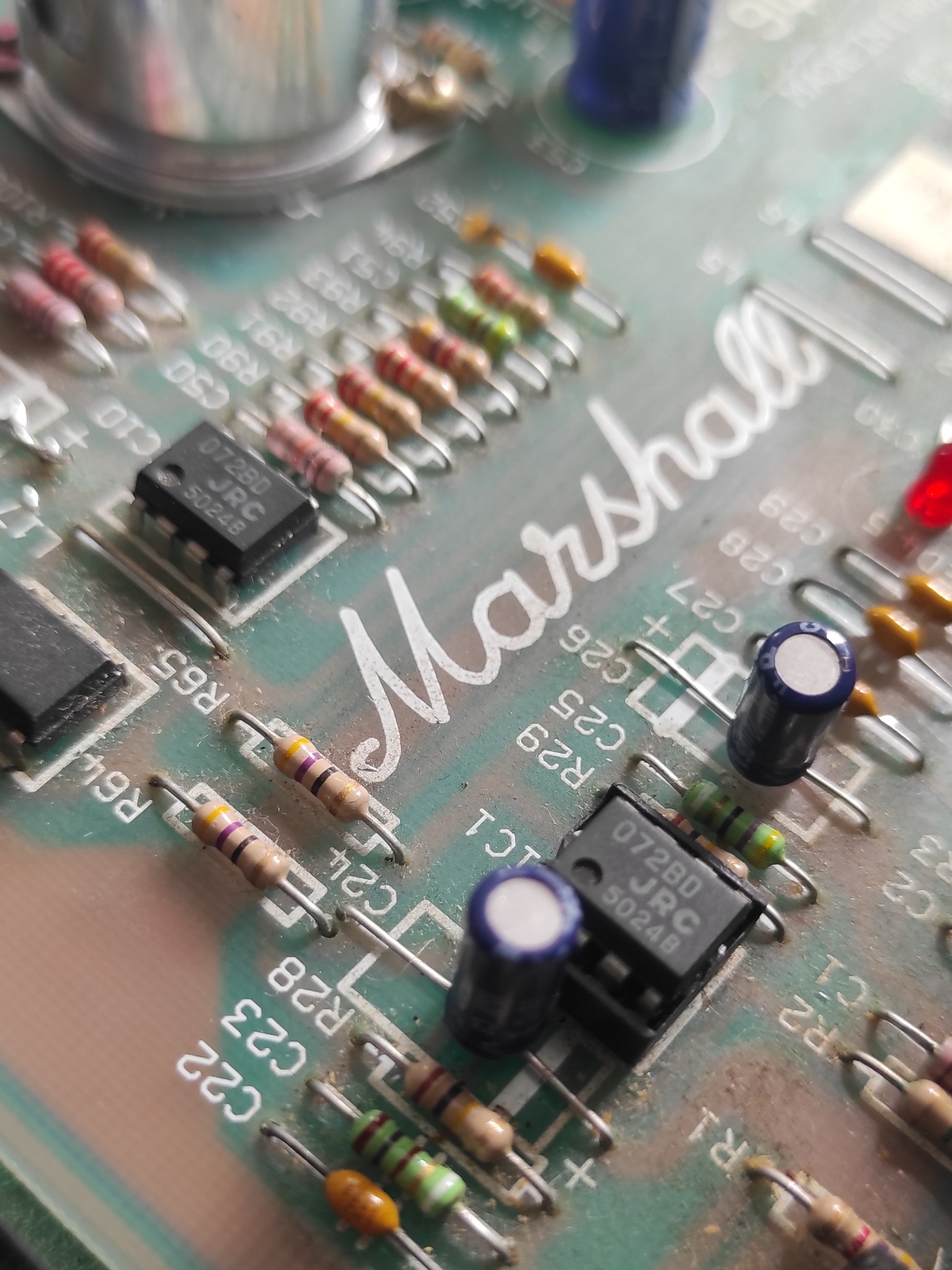 Zbliżenie na płytkę drukowaną Marshall z elementami elektronicznymi, takimi jak rezystory i układy scalone, z wyraźnym napisem marki.