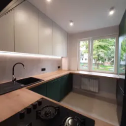 Nowoczesna kuchnia z zielonymi szafkami i drewnianym blatem. Widok na zieleń za oknem. Minimalistyczny design i funkcjonalne rozwiązania.