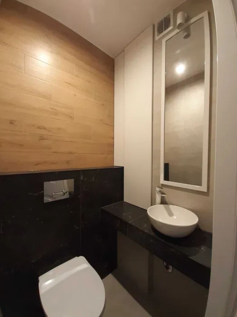 Nowoczesna łazienka z drewnianą boazerią i czarnym blatem z umywalką. Duże lustro w białej ramie optycznie powiększa przestrzeń.