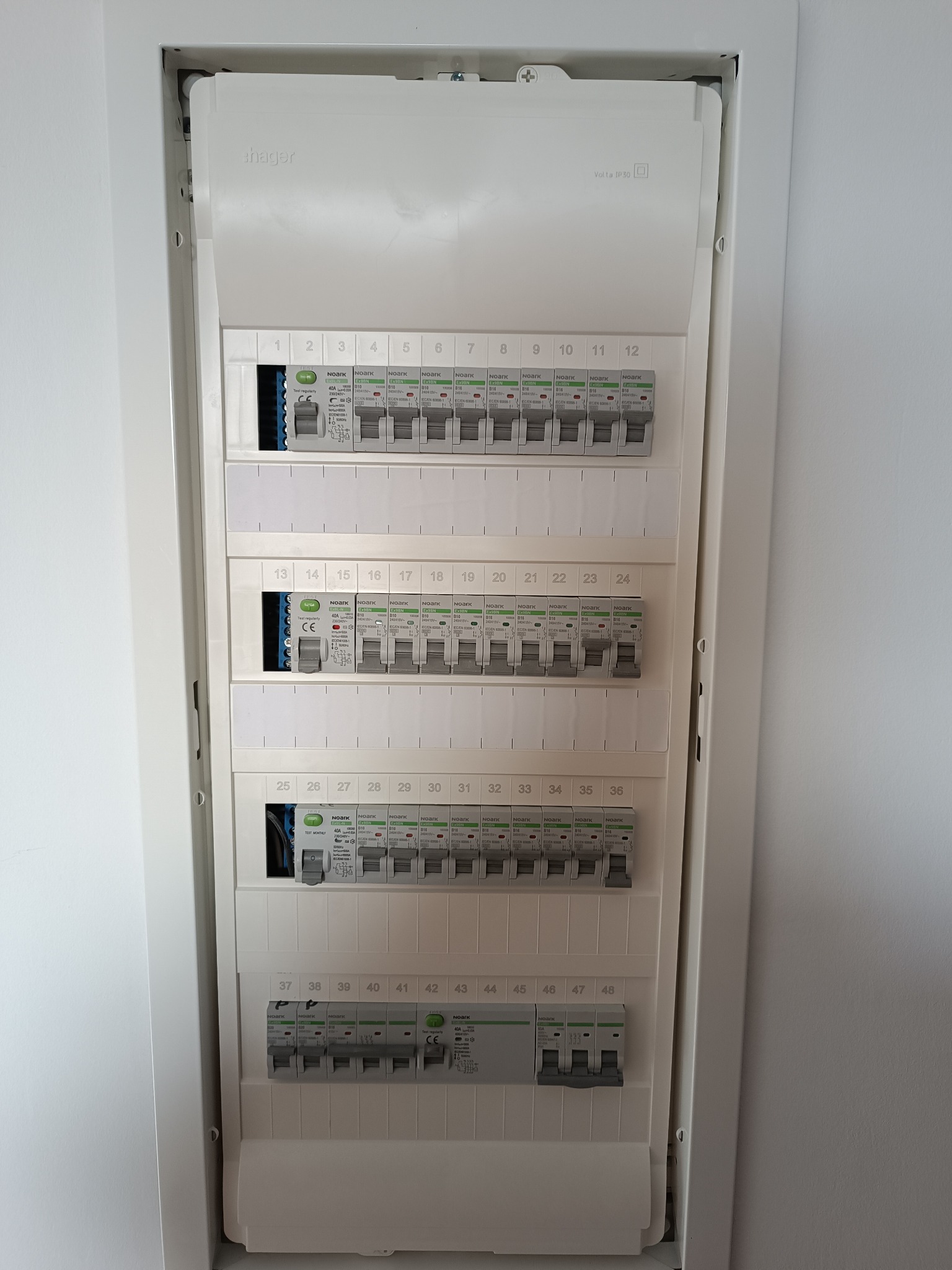 Rozdzielnica elektryczna Hager w białej obudowie, widok z przodu. Zabezpieczenia Noark B10 i B16, numery od 1 do 48. Montaż wnękowy, minimalistyczny design.