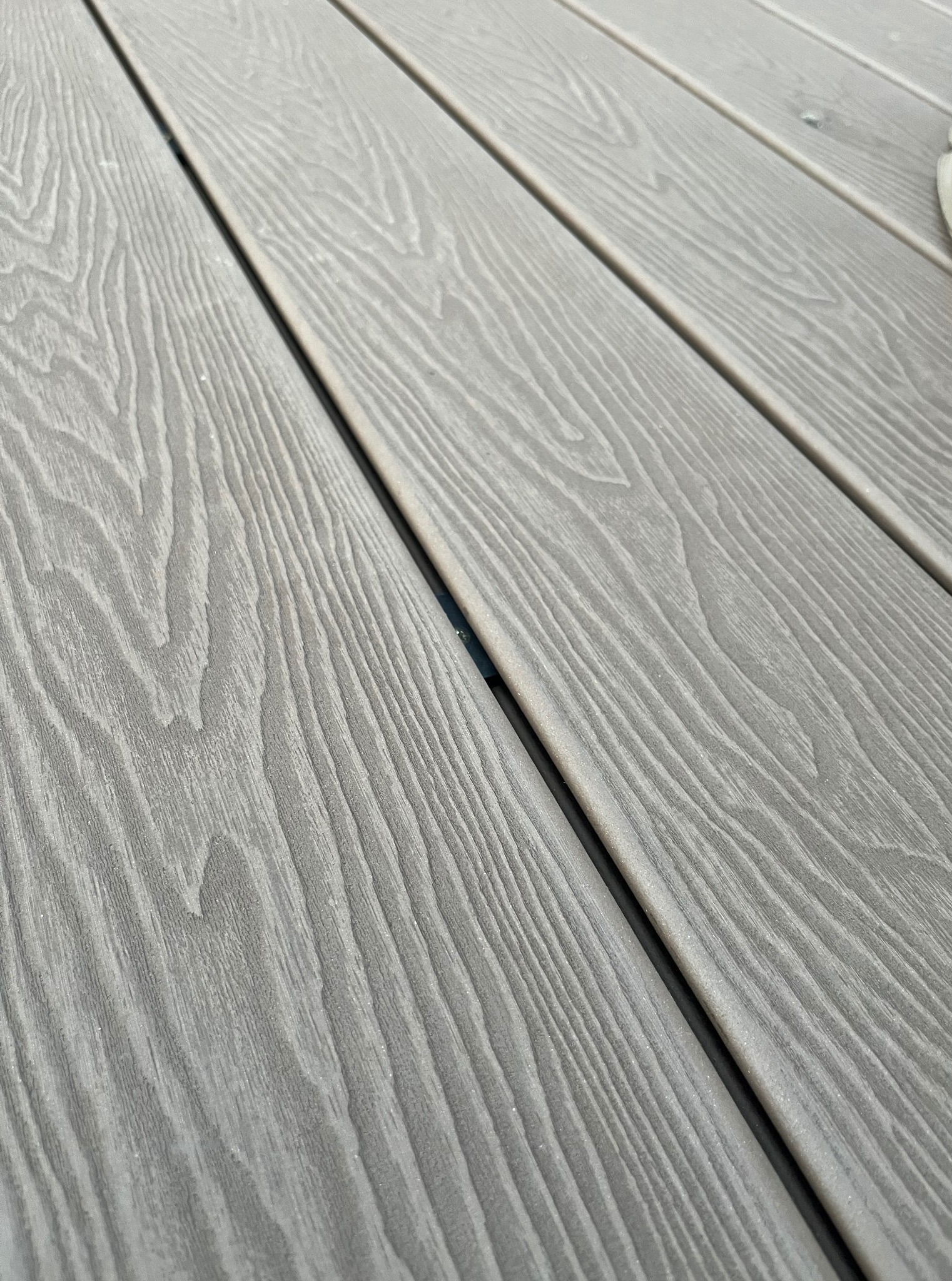 Szare deski kompozytowe tarasu, ułożone diagonalnie, z widoczną strukturą drewna i delikatnym cieniowaniem, podkreślającym głębię wzoru.