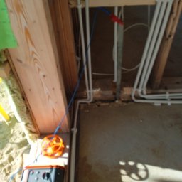 Rafał Marciniak - Pomiary instalacji elektrycznej w surowym wnętrzu. Widoczne przewody, miernik i elementy konstrukcji drewnianej. Niebieski przewód pomiarowy.