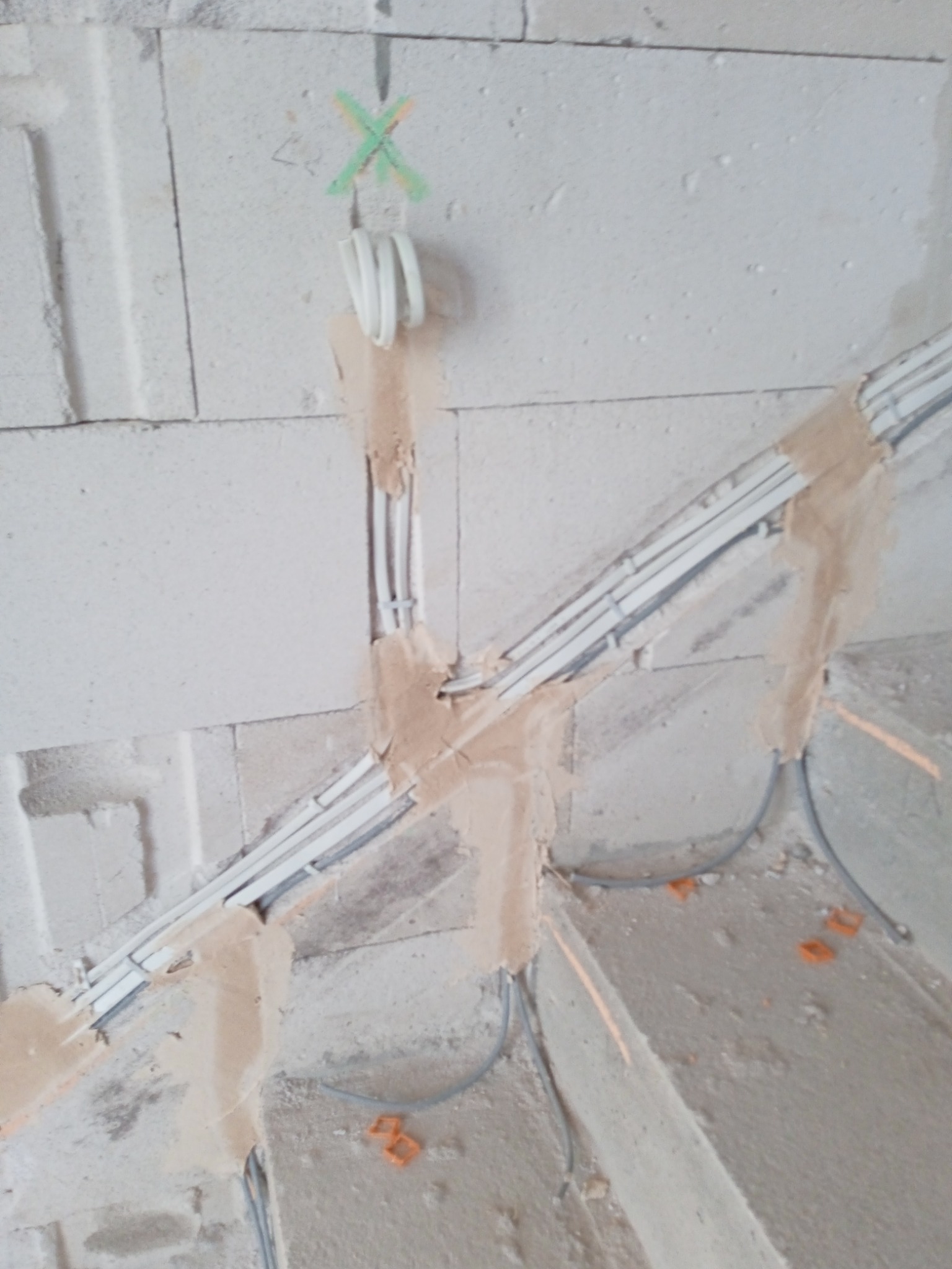 Wnętrze w trakcie prac: kable elektryczne ułożone w bruzdach ściany z betonu komórkowego, zamocowane gipsem. Zielony znak X nad jednym z kabli.