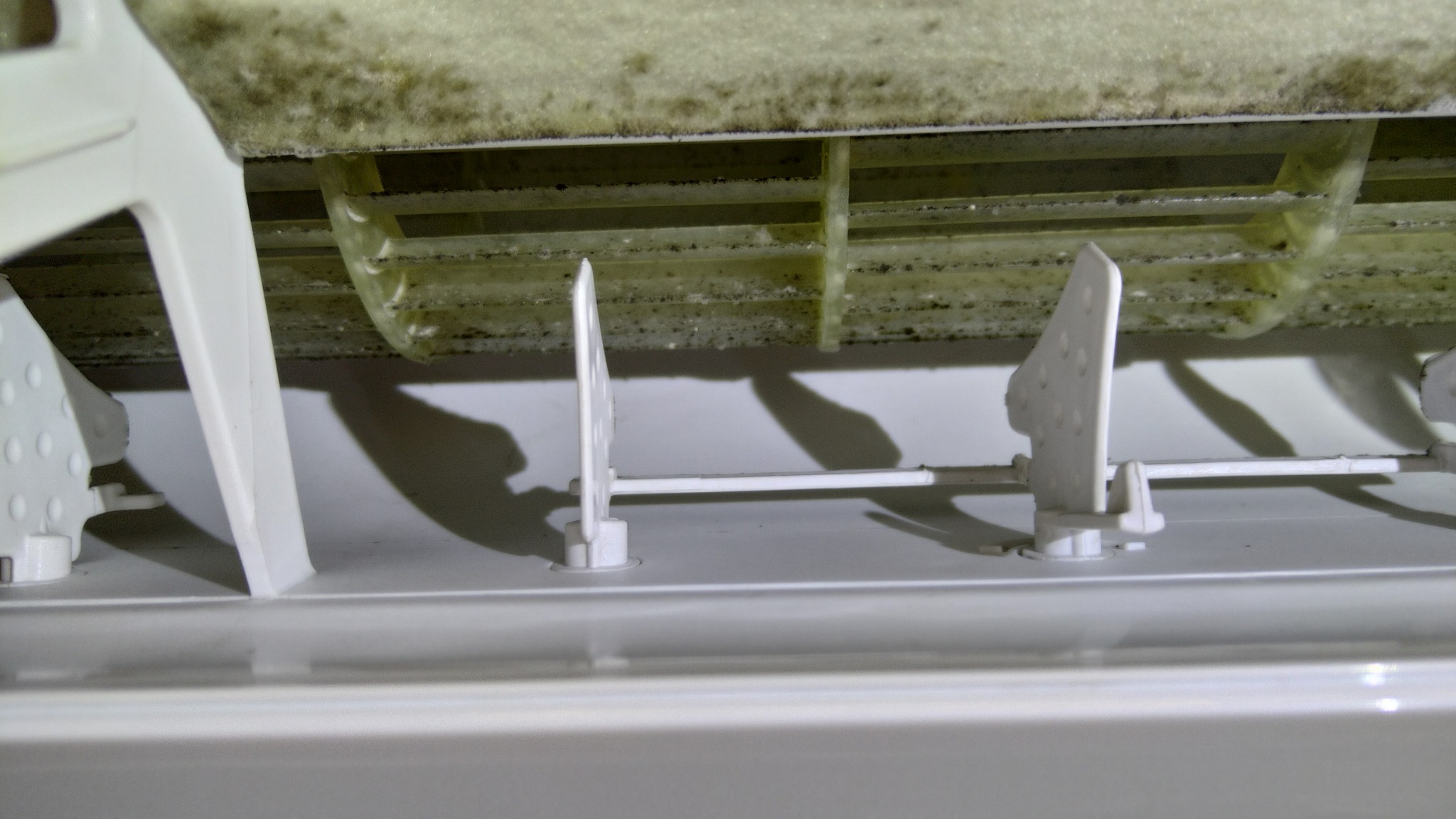 Zanieczyszczone wnętrze klimatyzatora z widocznym zagrzybieniem na filtrach i elementach konstrukcyjnych. Brak konserwacji urządzenia po dłuższym użytkowaniu.