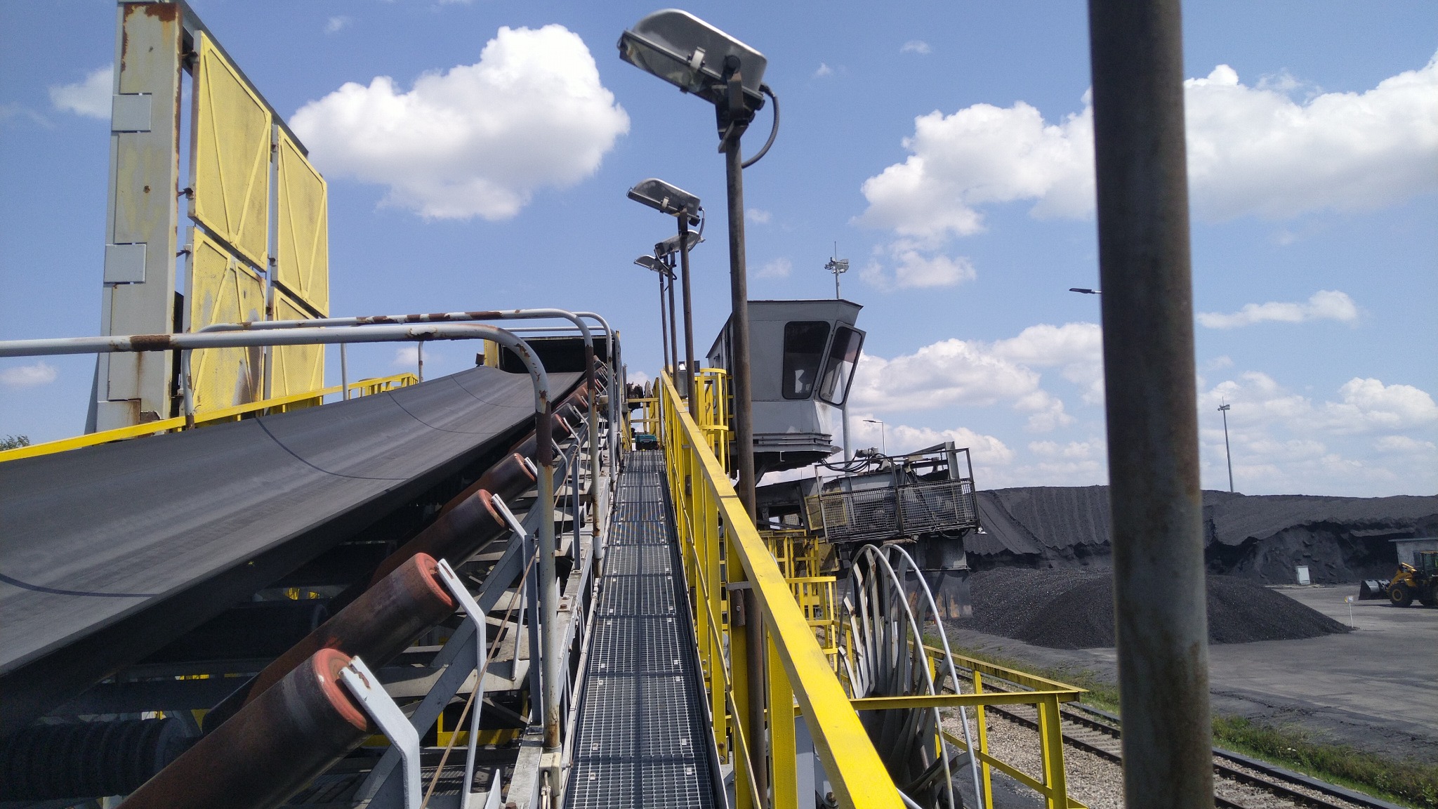 Widok na wózek załadowczy w kopalni Bogdanka z zamontowaną klimatyzacją. Szynowy wózek o długości dwóch TIRów, widoczne hałdy węgla i błękitne niebo z chmurami.