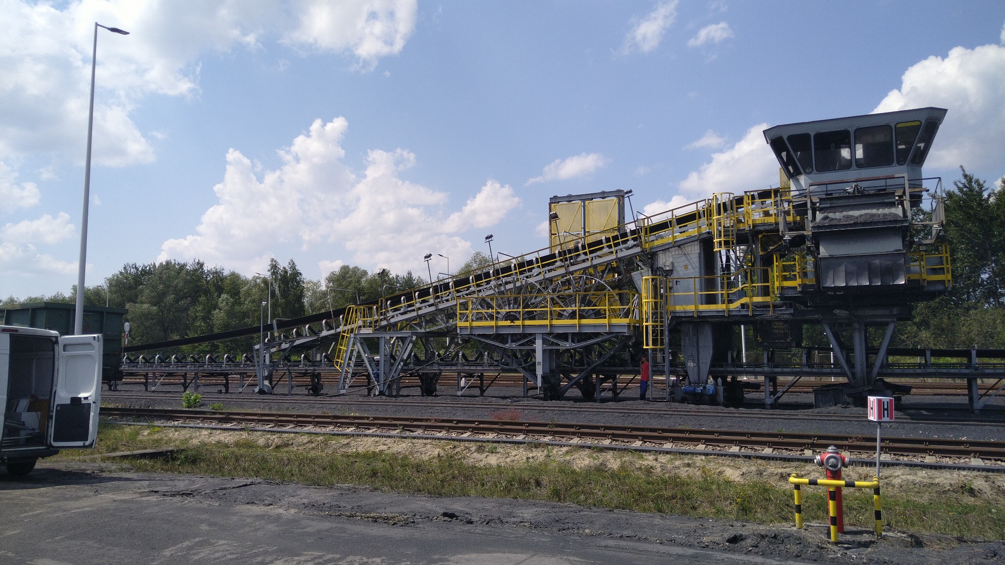 Szynowy wózek załadowczy w kopalni z zamontowaną klimatyzacją; widoczny fragment białego auta serwisowego i instalacja hydrantowa.