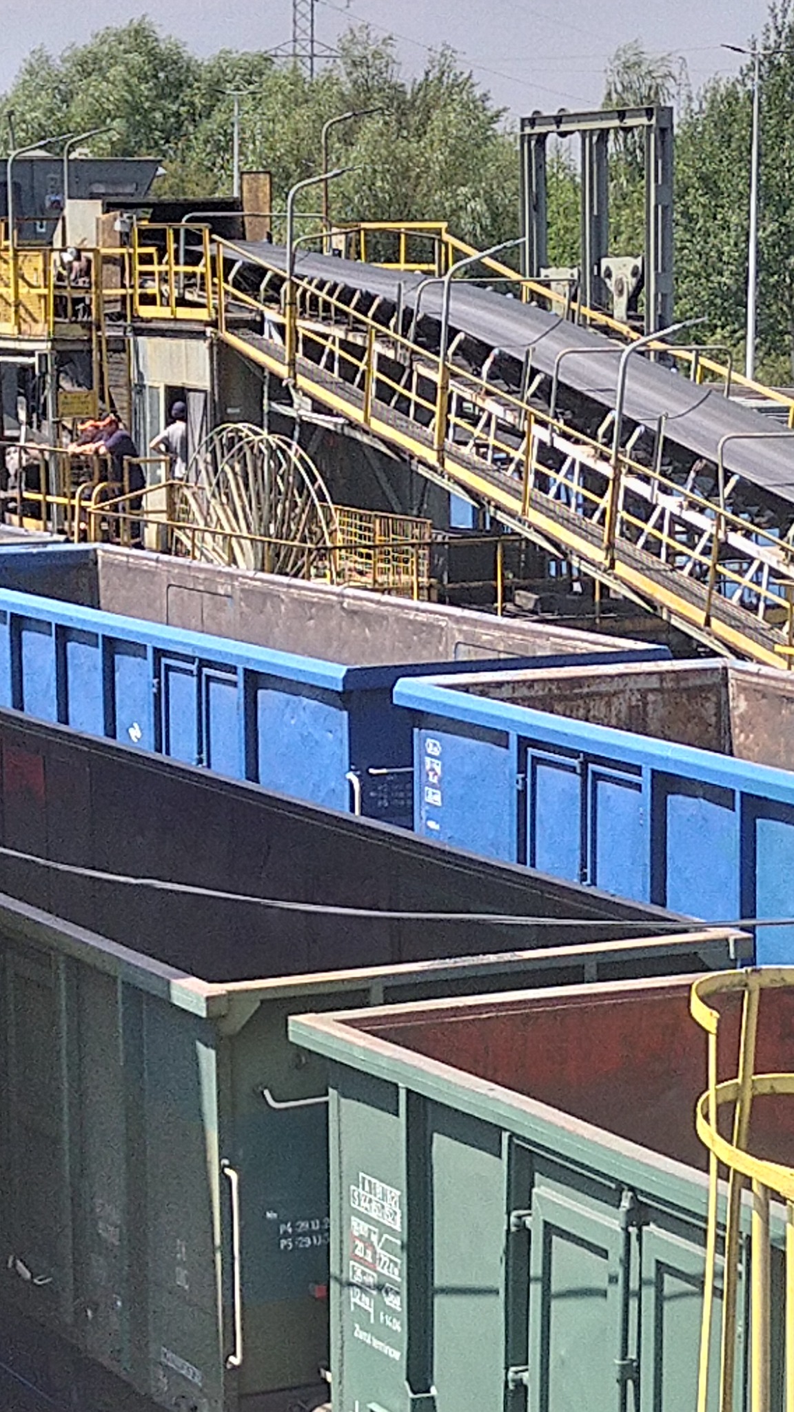 Montaż klimatyzacji w kopalni: Wózki szynowe z węglem, żółta konstrukcja podtrzymująca taśmociąg, pracownicy przy instalacji. Nietypowe miejsce instalacji.