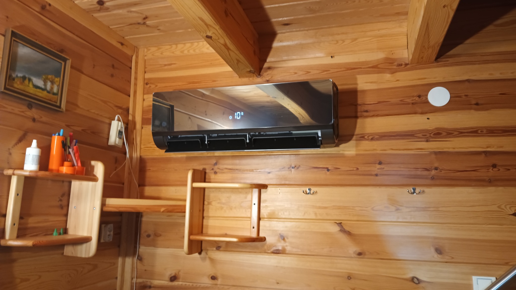 Czarny klimatyzator General Electric zamontowany na drewnianej ścianie domku letniskowego w Świdniku, z wyświetlaczem wskazującym 10 stopni Celsjusza.