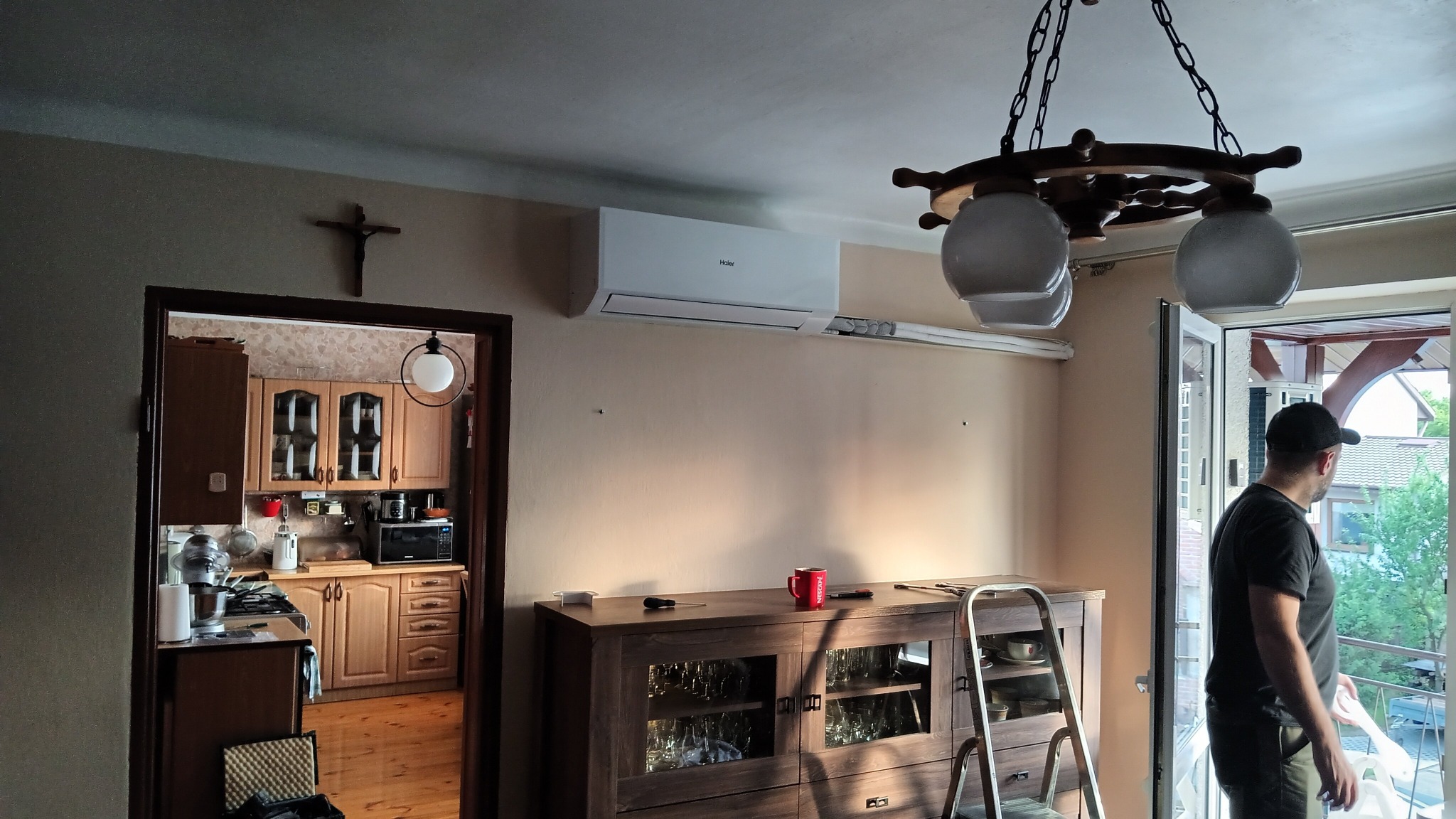Zamontowany klimatyzator Haier Revive w jasnym wnętrzu. Widoczna szafka, drabina i mężczyzna przy otwartym balkonie. Uwagę zwraca lampa w stylu marynistycznym.
