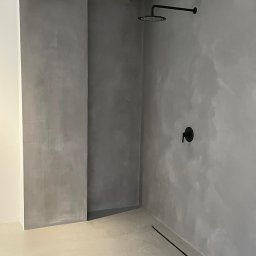 Pracownia Usługowa Agata Binkowska - Minimalistyczna kabina prysznicowa z szarą, gładką powierzchnią ścian i podłogi, czarną armaturą i odpływem liniowym. Nowoczesne wykończenie wnętrza łazienki.