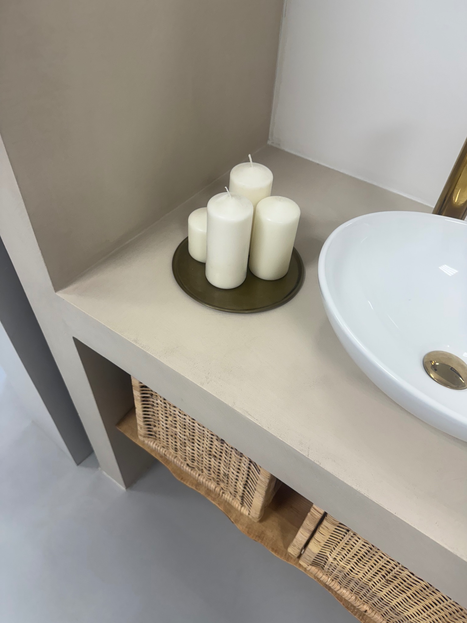 Wykończona łazienka z umywalką nablatową, świecami i wiklinowymi koszami. Beżowe ściany i podłoga z mikrocementu. Minimalistyczny design.