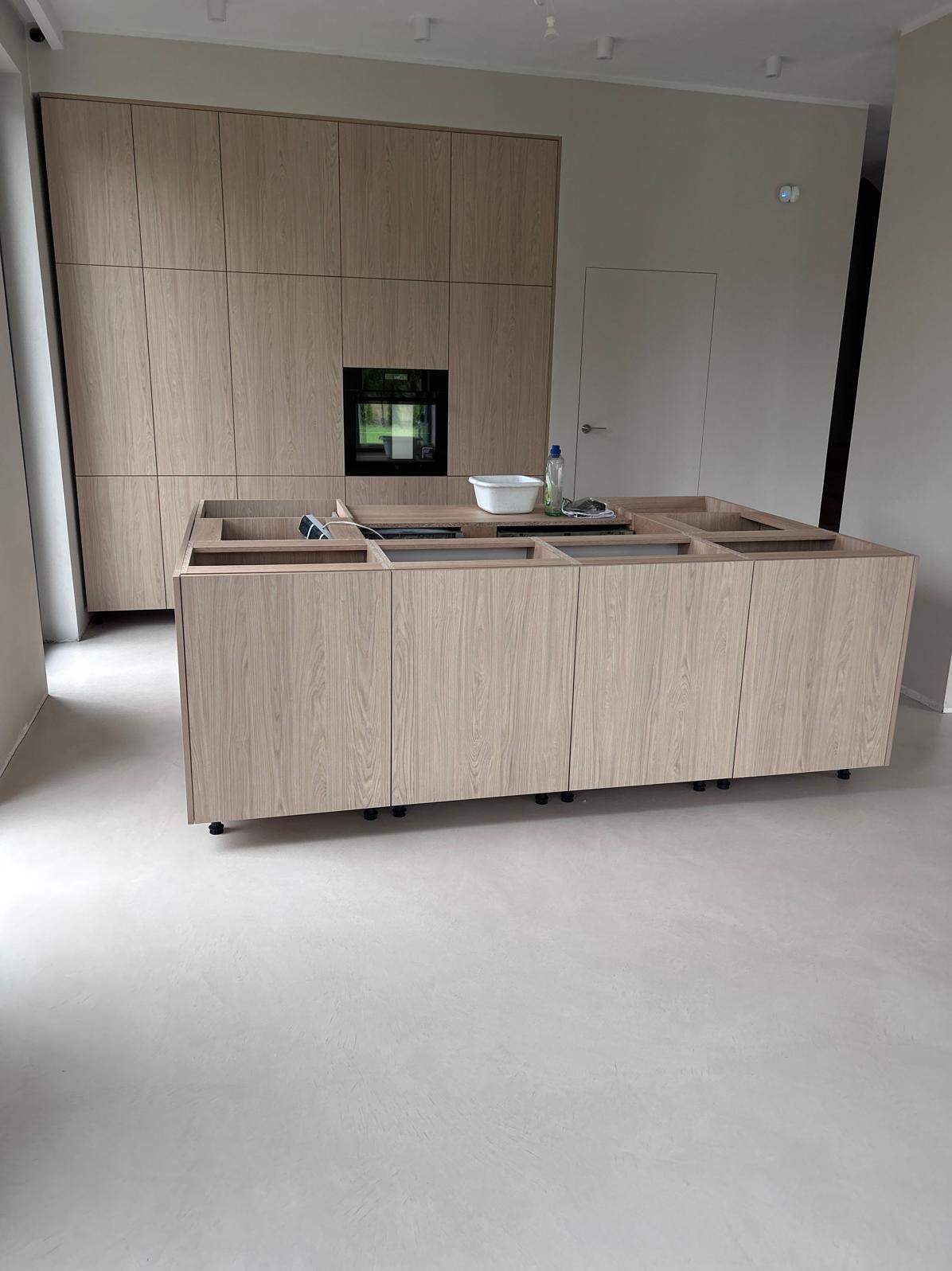 Jasna, gładka posadzka w nowoczesnej kuchni z drewnianą zabudową i wyspą. Widoczne detale montażowe wyspy kuchennej.