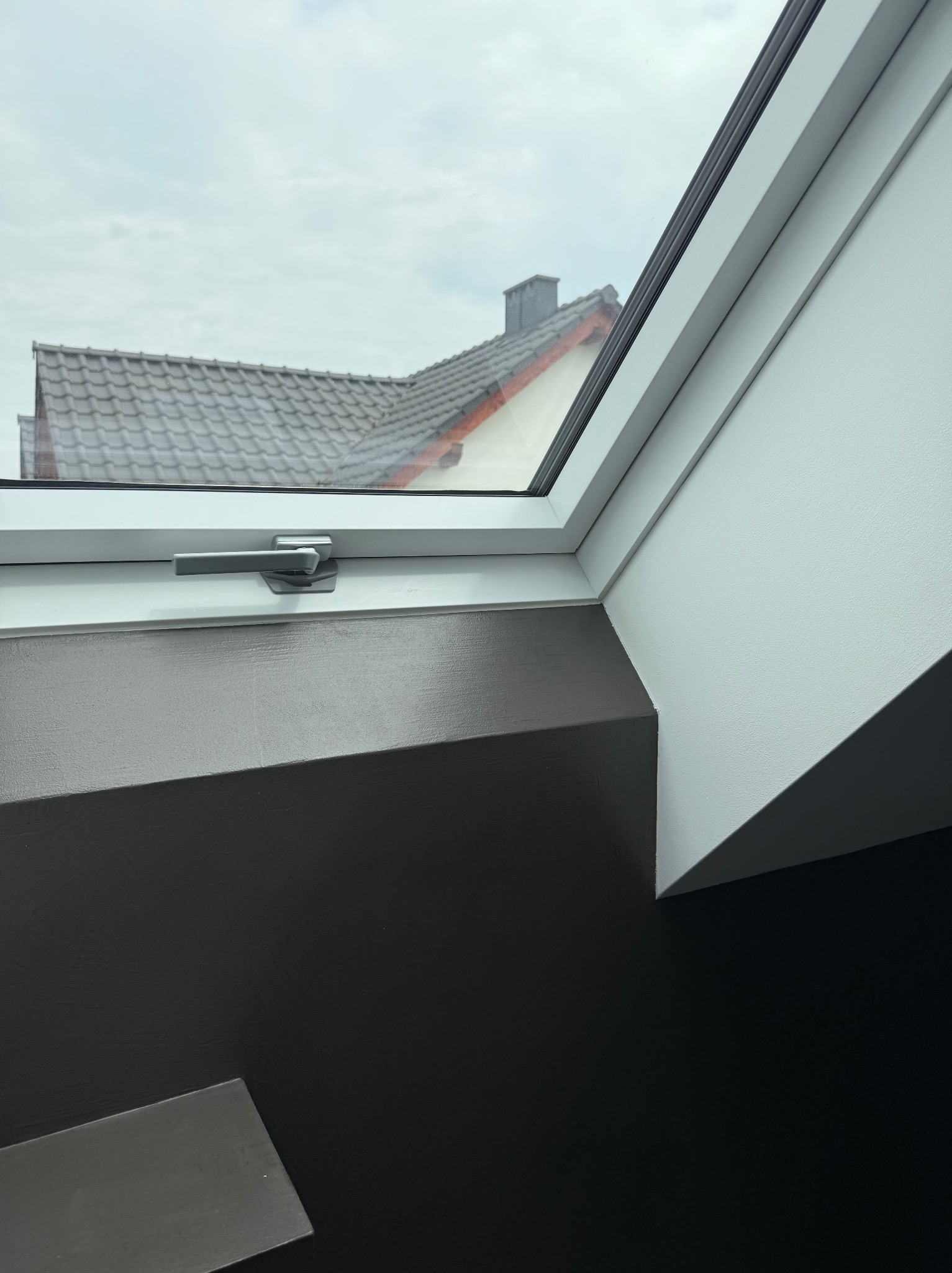 Szare ściany przy białym oknie dachowym z widokiem na dach domu. Kontrastowe wykończenie wnętrza, nowoczesny design.