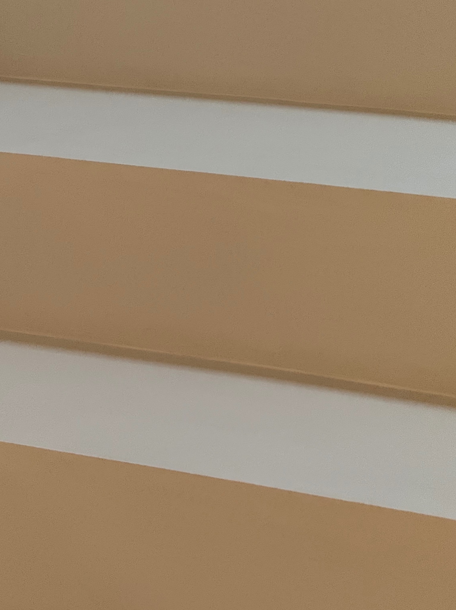 Fragment ściany z poziomymi pasami w odcieniach beżu i bieli, ukazujący fakturę i wykończenie powierzchni. Ujęcie z bliska, podkreślające detale.
