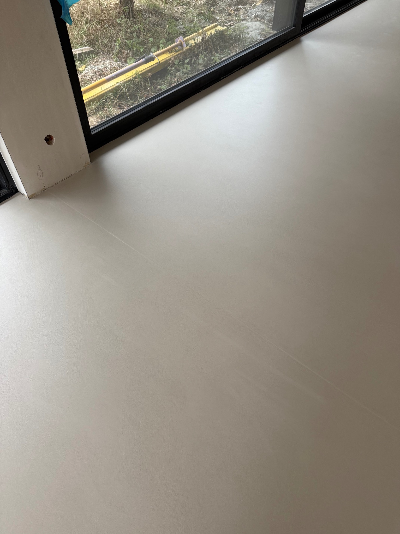 Jasna, gładka posadzka w nowym wnętrzu, widoczna przy oknie z czarną ramą. Minimalistyczny design, świeżo wylana powierzchnia, delikatna faktura. Widok z góry.