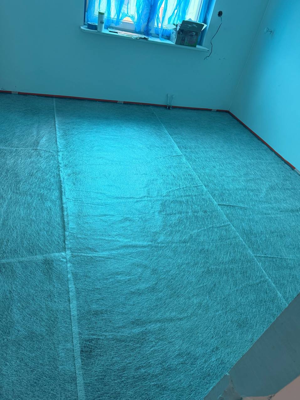 Przygotowanie podłoża pod wylewkę: rozłożona siatka wzmacniająca na podłodze w pomieszczeniu przed dalszymi pracami wykończeniowymi. Widoczne okno i fragment ściany.