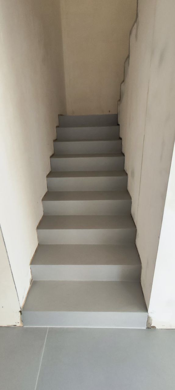 Szare schody w surowym wnętrzu, świeżo po wykończeniu. Widoczne niedoskonałości ścian i podłogi, podkreślające minimalistyczny charakter przestrzeni.
