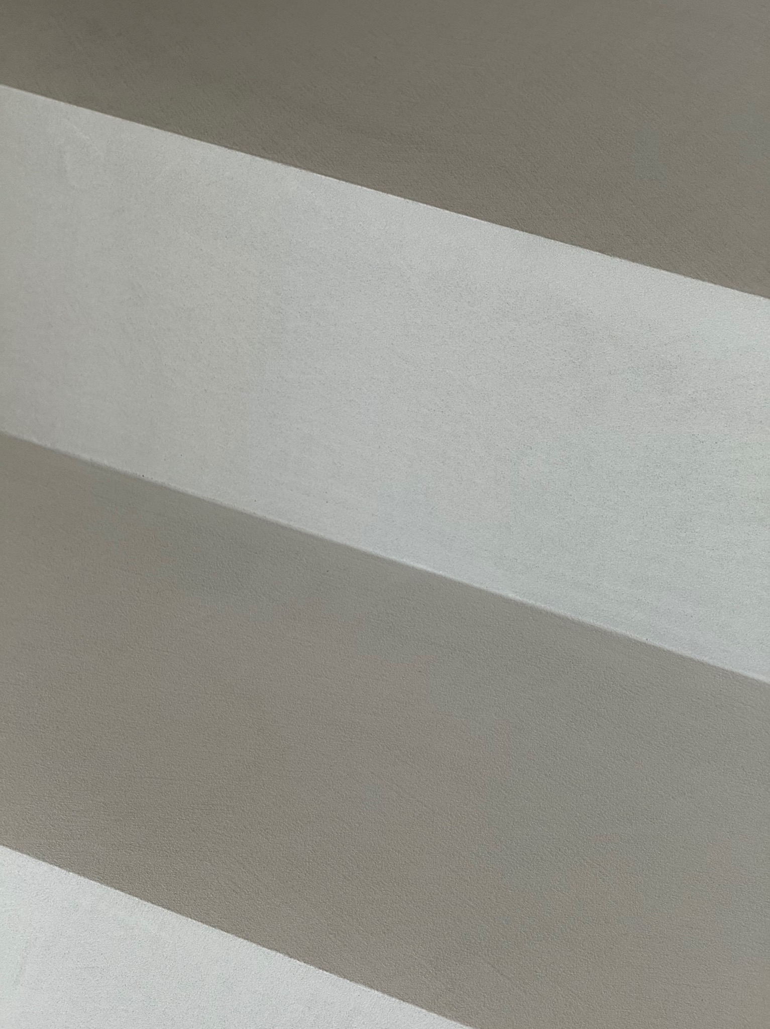 Minimalistyczne ujęcie fragmentu ściany z efektem cieniowania, ukazujące fakturę i gładkie wykończenie w odcieniach szarości. Delikatne światło podkreśla strukturę powierzchni.