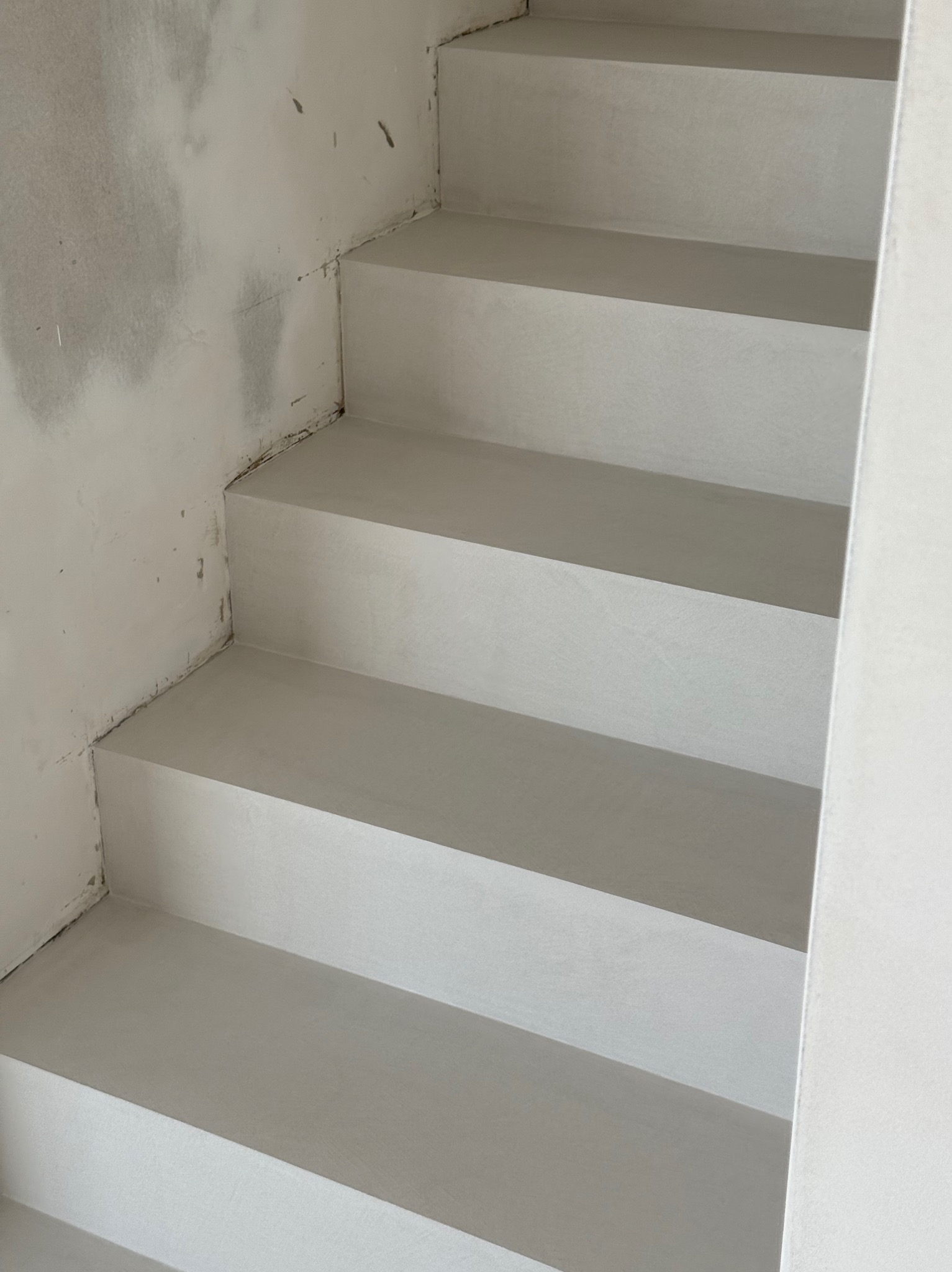 Schody wykończone w jasnym odcieniu szarości, widoczne z bliska w Trzebnicy. Minimalistyczny design, gładka powierzchnia, surowe ściany w tle.