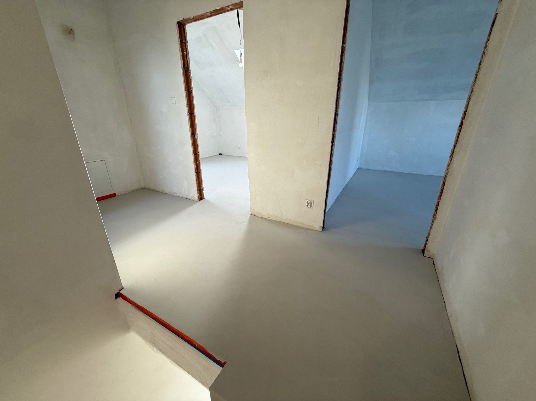 Jasnoszara, gładka posadzka w surowym wnętrzu z widocznymi otworami drzwiowymi i fragmentami ścian. Minimalistyczny design, świeżo wylana powierzchnia.