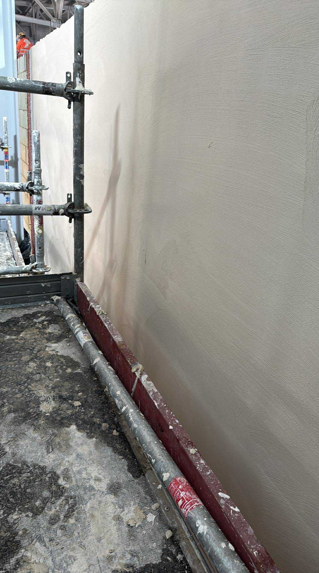 Świeżo nałożony tynk na ścianie, widoczny z bliska ze stojącego rusztowania, z delikatną fakturą i subtelnym oświetleniem.